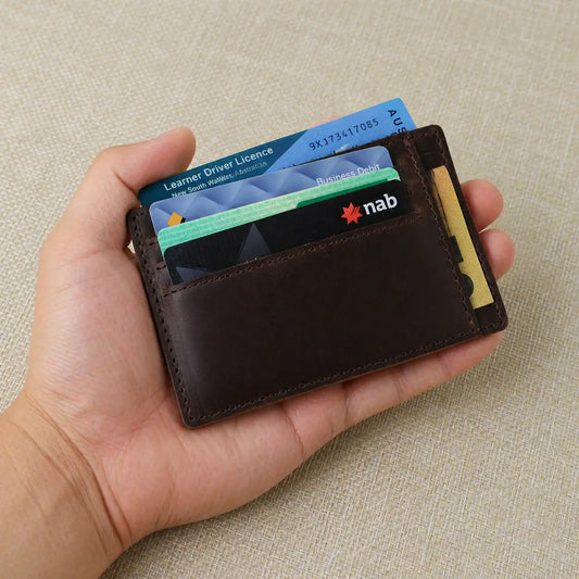 A person holding a dark brown pebbled leather wallet with a personalized name engraving and visible perimeter stitching.