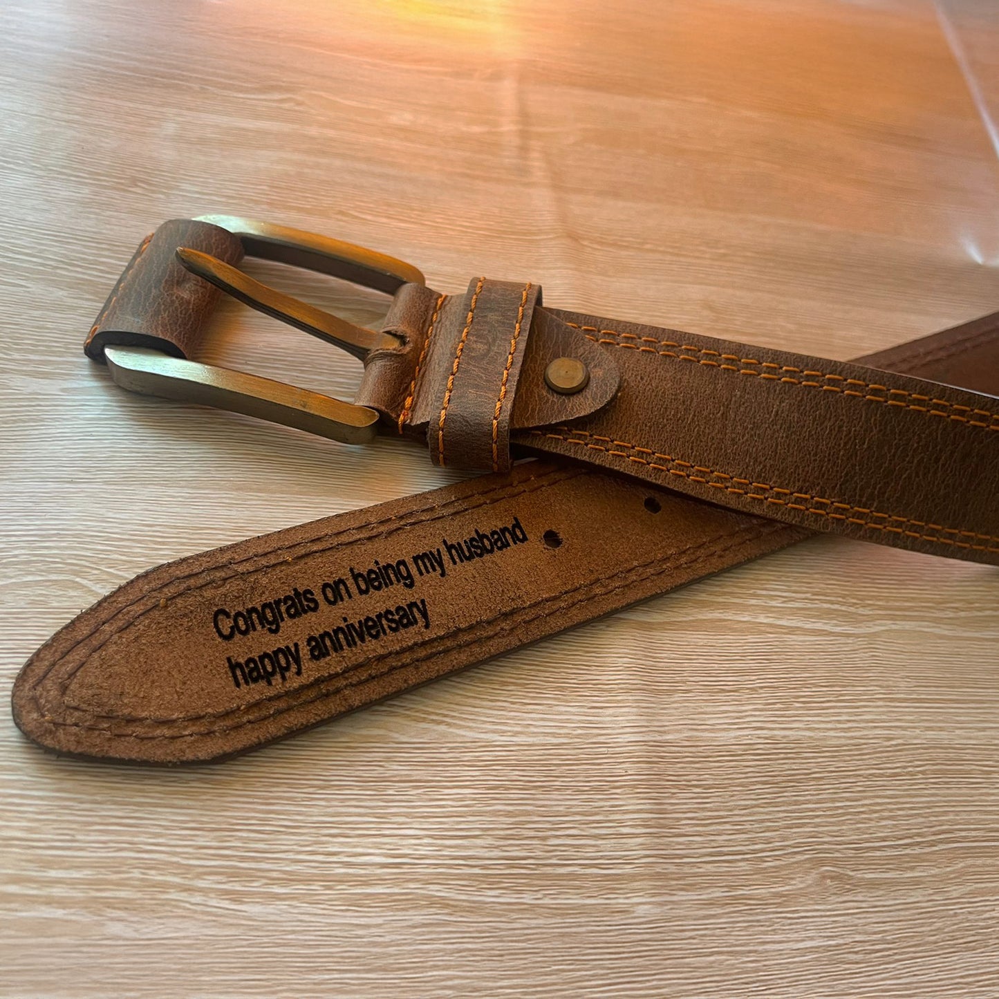 Brown leather belt with engraved message on a wooden surface