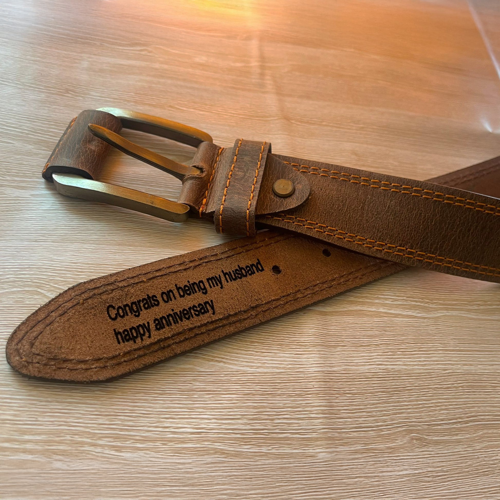 Brown leather belt with engraved message on a wooden surface