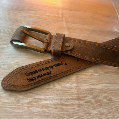 Brown leather belt with engraved message on a wooden surface