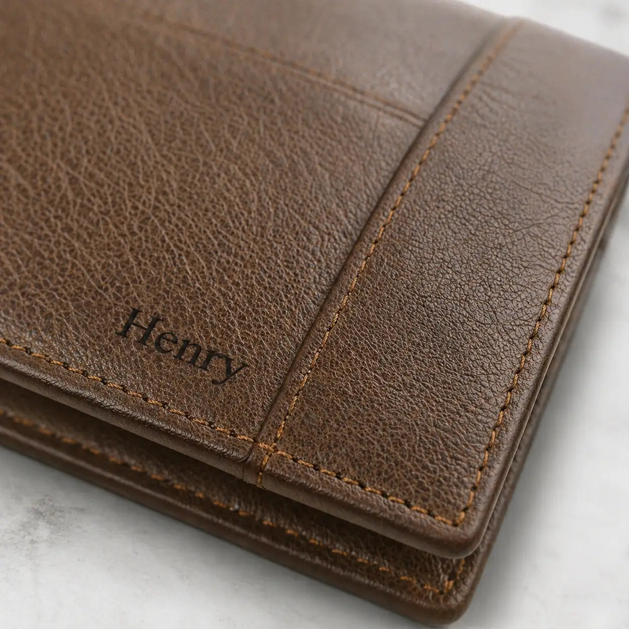 Close-up of a personalized brown grain leather wallet featuring the name "Henry" custom-engraved in a classic serif font.