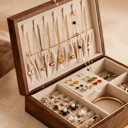 Close-up luxury walnut jewelry organizer with soft beige velvet interior featuring neatly arranged gold necklaces, rings, earrings and bracelet compartments in warm elegant lighting.