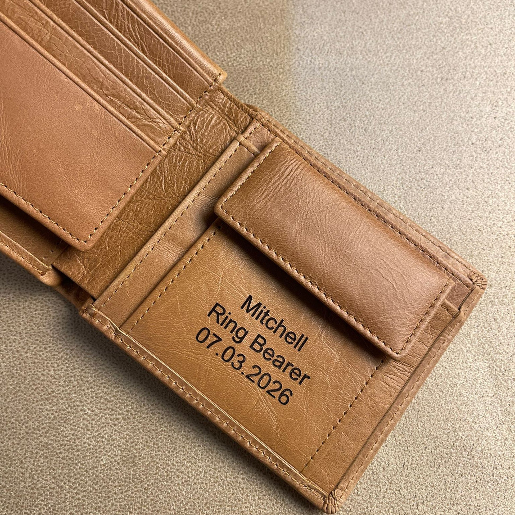 Interior view of a high-quality tan leather trifold wallet showing organized card slots, a snap coin compartment, and personalized laser engraving for wedding party gifts.