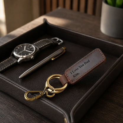Personalised brown leather keychain with antique brass ring styled beside watch and keys on a black valet tray