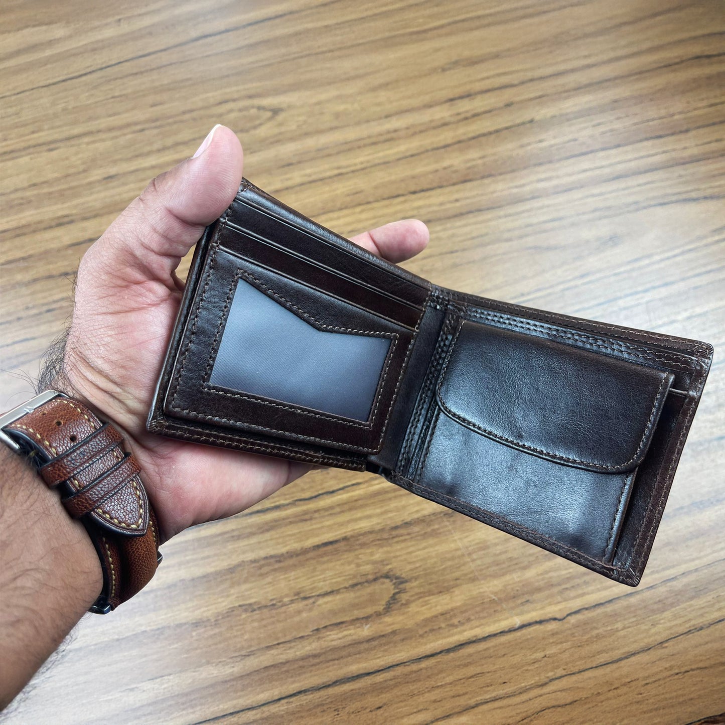 Hand holding an open brown leather wallet on a wooden surface