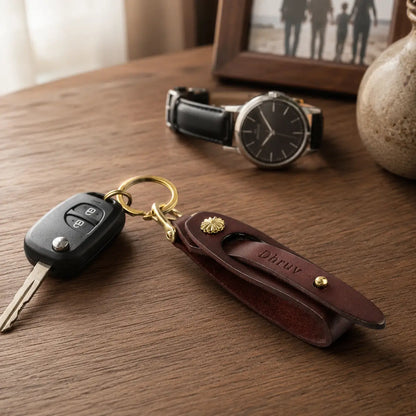 Brown leather key holder with attached car key displayed beside wristwatch on a wooden desk