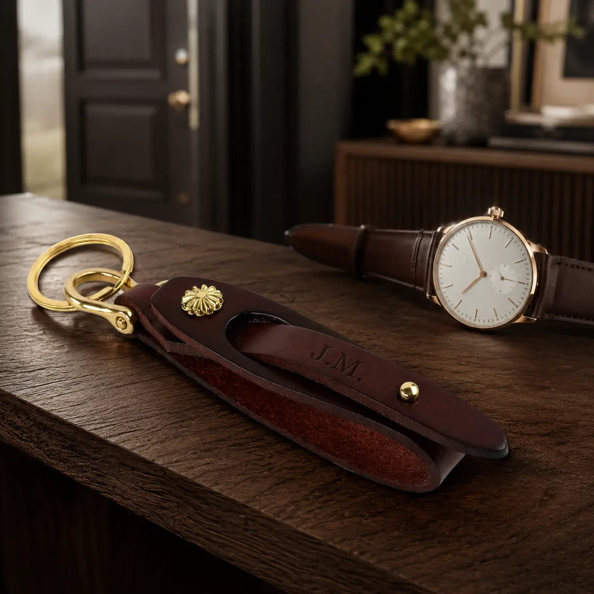 Brown leather key holder with brass key ring styled beside white dial wristwatch on wooden surface