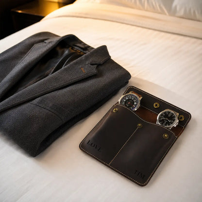 Dark brown personalized leather double watch pouch placed on a luxury hotel bed beside a folded blazer with warm ambient lighting and elegant travel lifestyle styling.