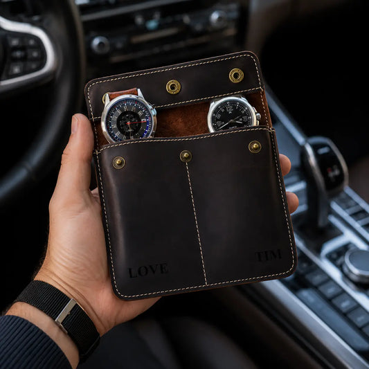 Dark espresso brown leather double watch pouch held in a man’s hand inside a luxury car interior with two watches visible, beige stitching, brass buttons, and premium masculine travel aesthetic.