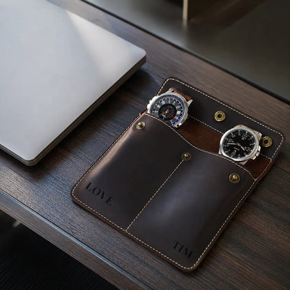 Dark espresso brown leather double watch pouch with two watches placed on a modern executive desk beside a closed laptop in a clean luxury workspace setting.