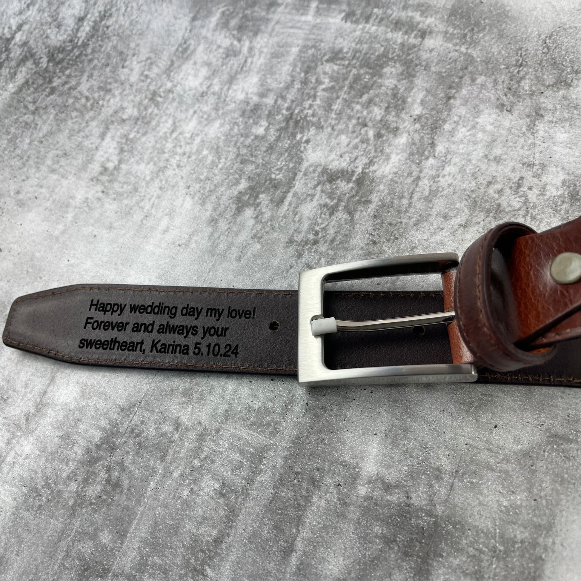 Brown leather belt with engraved message on a gray surface