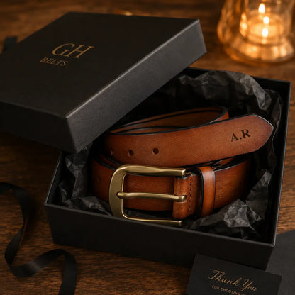 Alt text: Personalized brown genuine leather belt with antique brass buckle displayed inside a premium black gift box with black tissue paper, engraved initials visible, luxury gift presentation with warm ambient lighting.