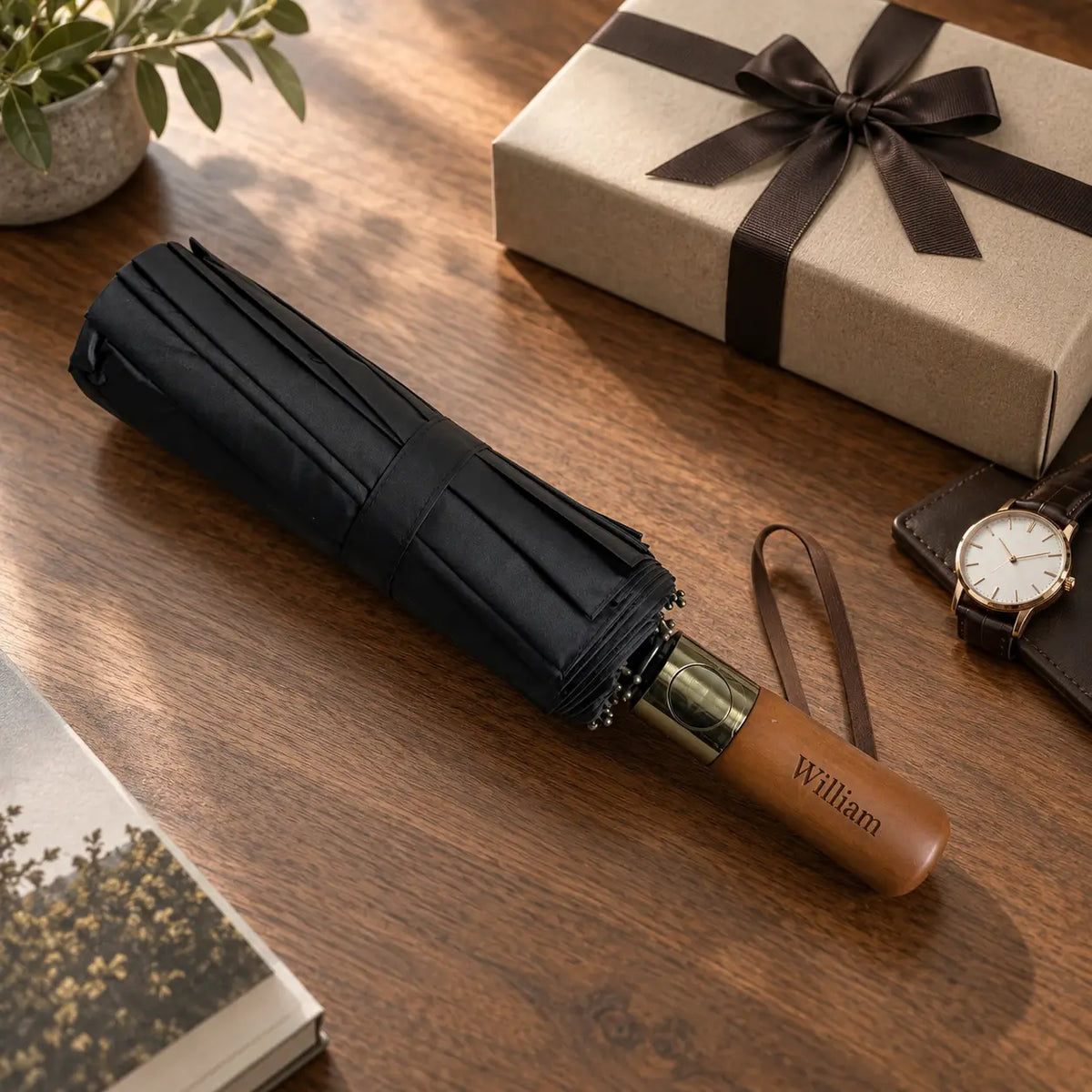 Personalised black folding umbrella with wooden handle engraved William beside gift box on wooden table