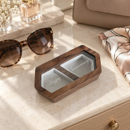 Personalised wooden ring box with engraved glass or lid displayed beside sunglasses and a handbag on a neutral dressing table.