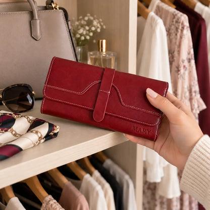 Personalised burgundy women’s wallet engraved with MARY held in hand beside handbag and fashion accessories