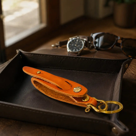 Orange leather key holder with brass hardware displayed on a black valet tray beside wristwatch