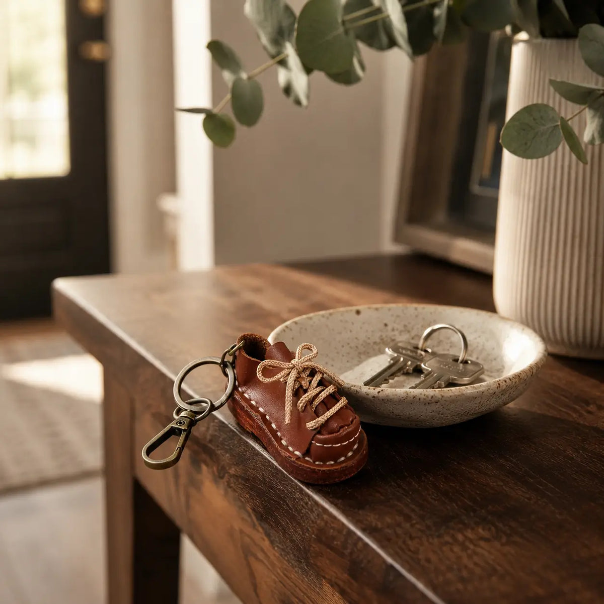 Brown leather shoe keychain styled beside wristwatch and keys on a wooden bedside table