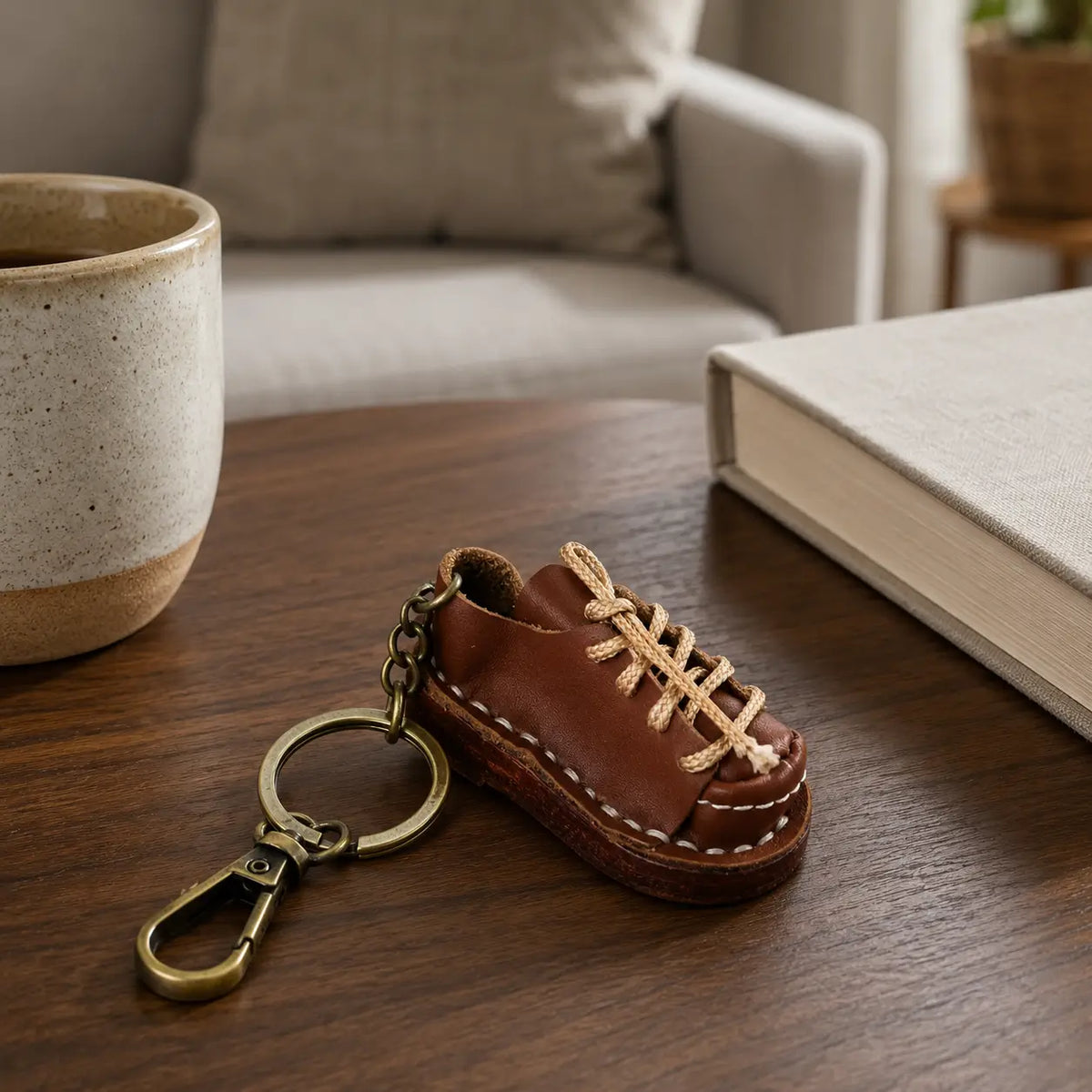 Brown leather shoe keychain styled beside coffee cup and books on a wooden table
