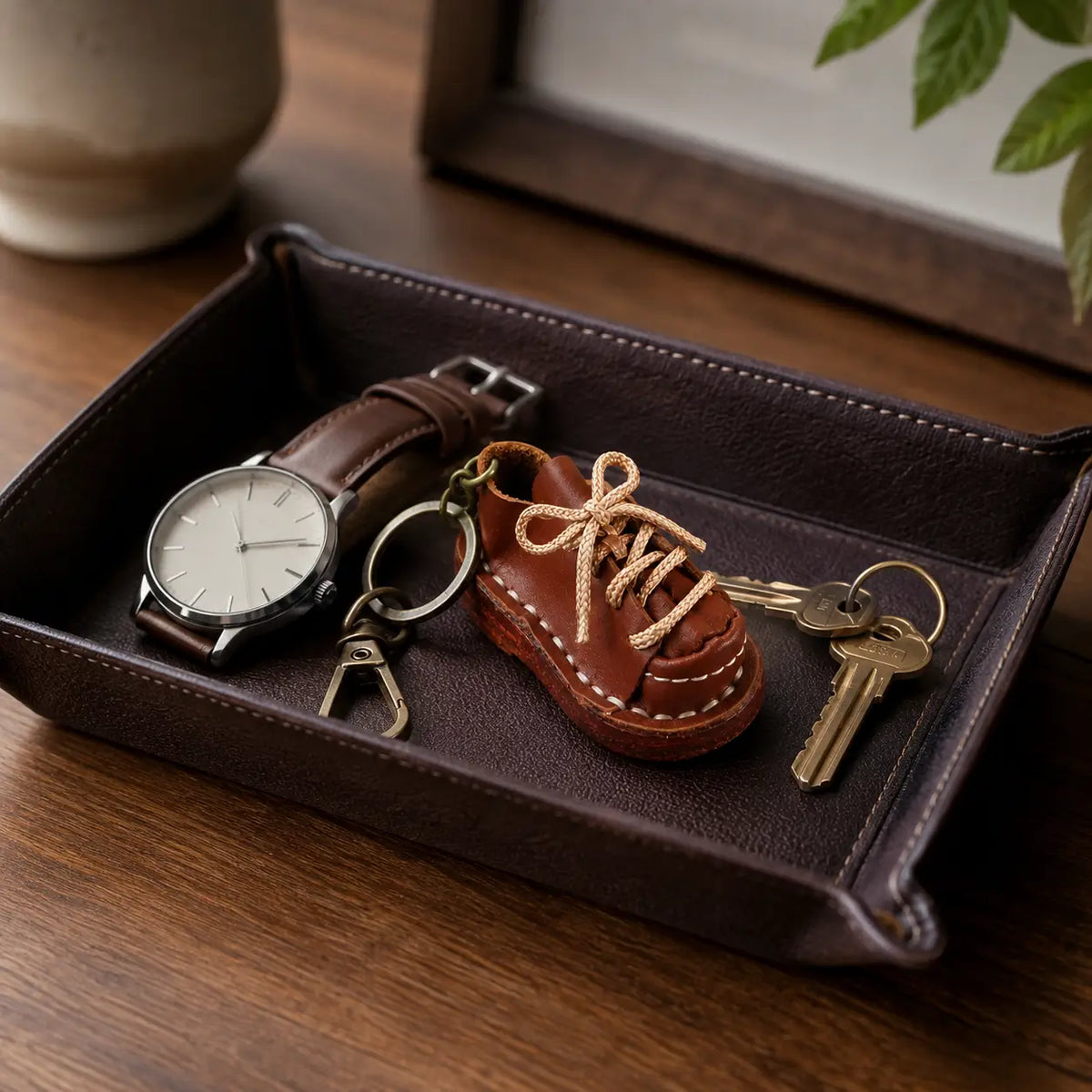 Brown leather shoe keychain displayed in a dark leather valet tray with watch and keys