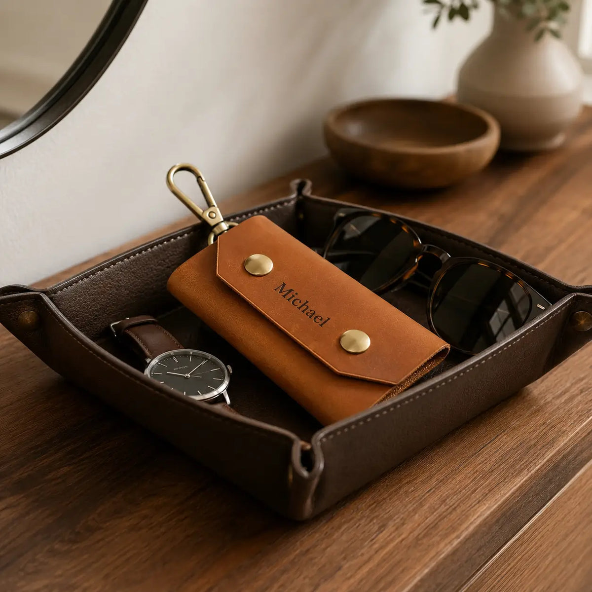 Tan leather key case with brass hardware displayed inside a valet tray beside watch and accessories