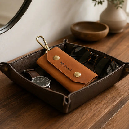 Tan leather key case with brass hardware displayed inside a valet tray beside watch and accessories