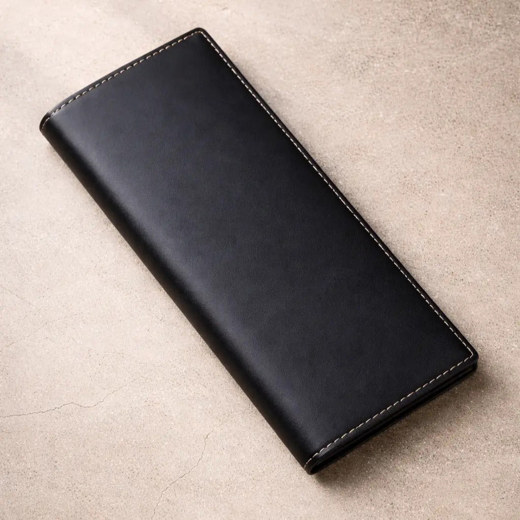 Men's black leather breast pocket wallet with a minimalist bifold design and durable handcrafted stitching, shown on a neutral stone surface.