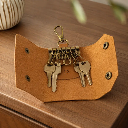 Open tan leather key holder showing multiple key hooks and attached keys on a wooden table