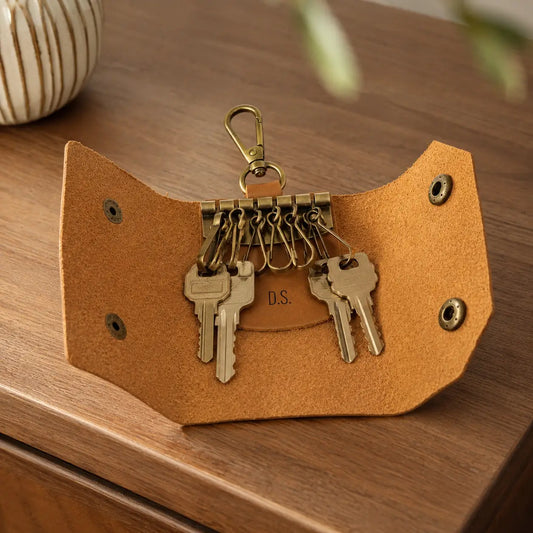 Open tan leather key holder showing multiple key hooks and attached keys on a wooden table