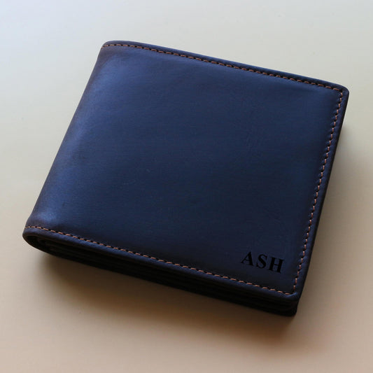 Dark brown leather wallet with 'ASH' monogram engraved on it on a beige background