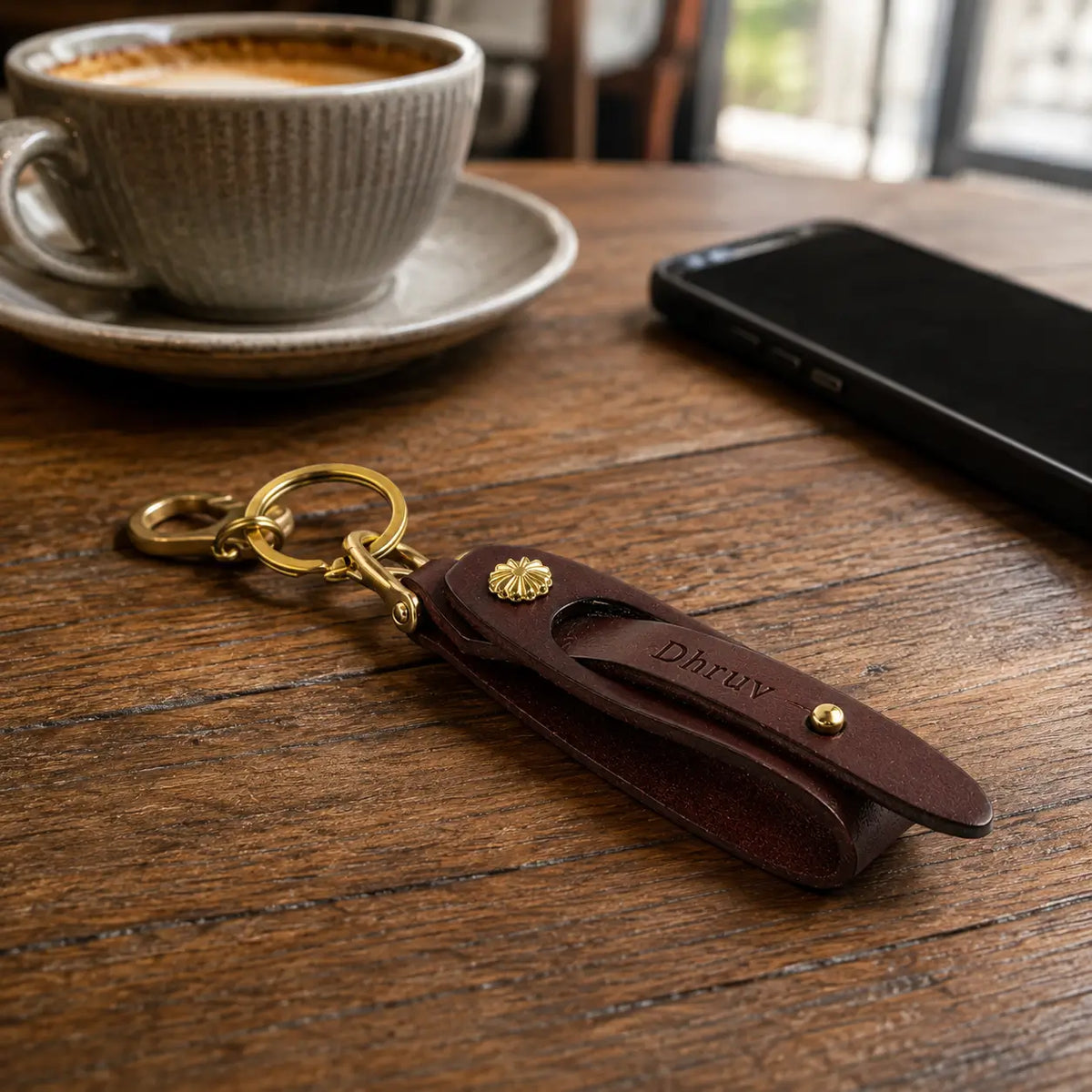 Brown leather key holder displayed beside coffee cup and smartphone on a wooden table