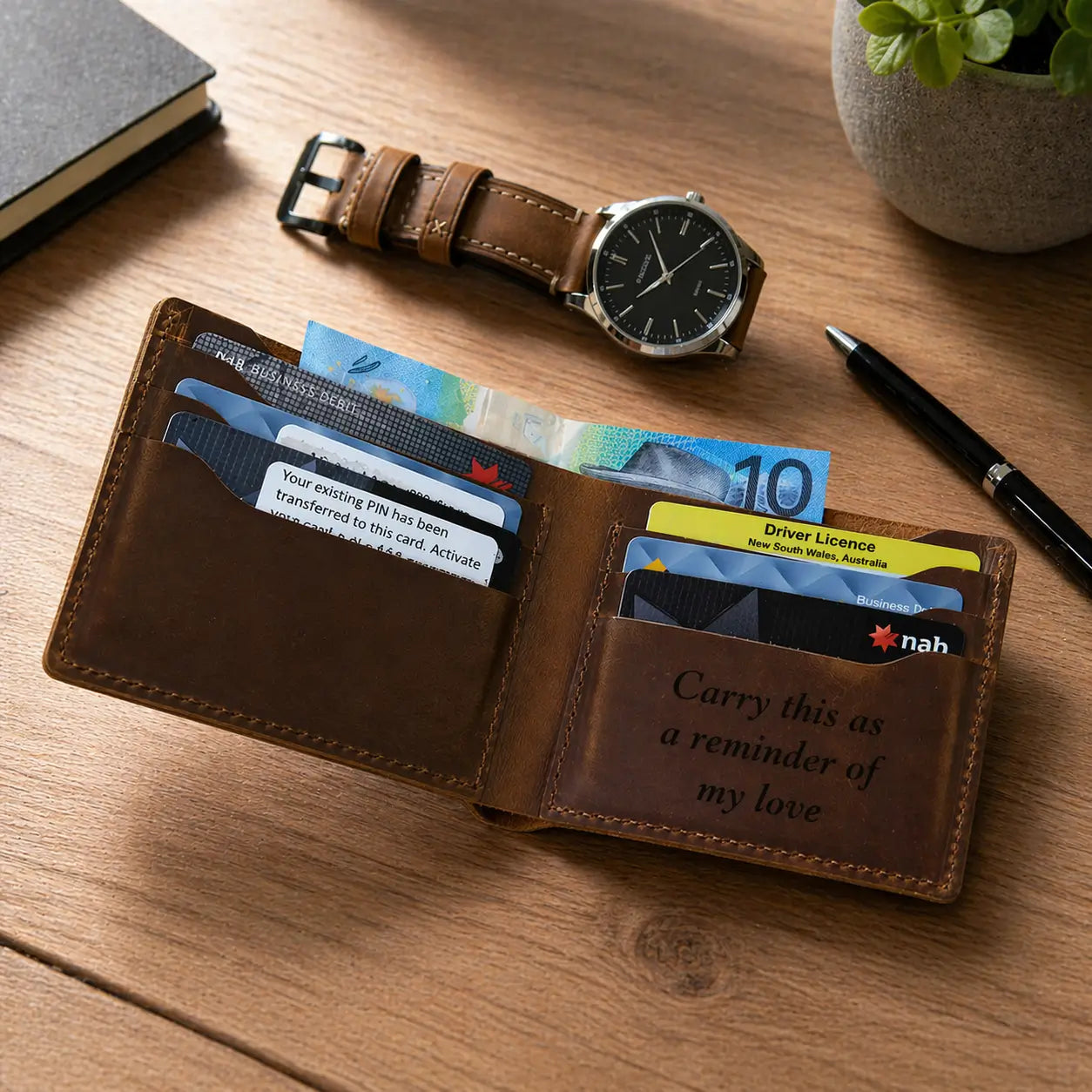 Custom engraved men's leather wallet in tan brown, featuring laser-etched "Carry this as a reminder of my love" text, multiple card slots, and matching leather watch strap on a wooden desk.
