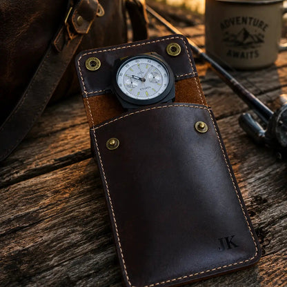 Dark brown personalized leather watch pouch with a partially visible watch resting on a rustic wooden surface during sunset beside a leather travel bag and outdoor adventure setup with warm golden lighting.