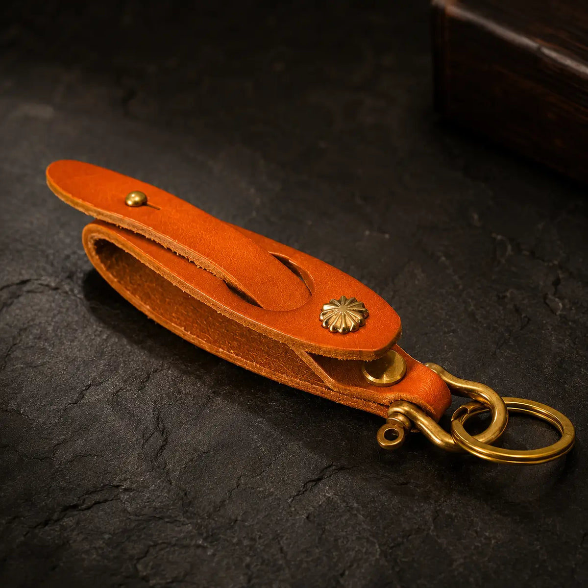 Orange leather key holder with antique brass key ring and snap fastenings photographed on a dark textured background