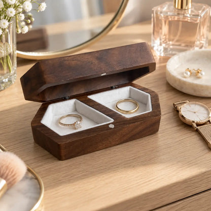Dark walnut double ring box with engagement and wedding rings displayed beside candlelight in a romantic wedding setting.