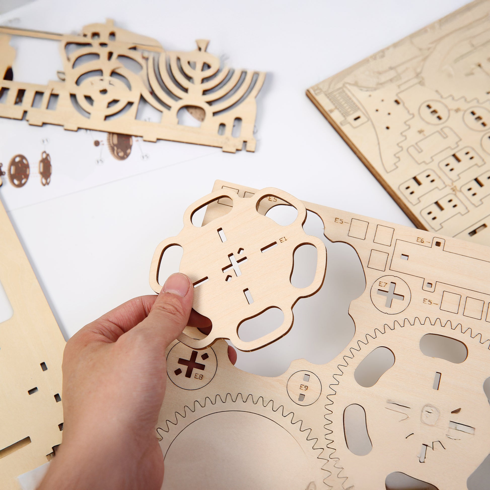 Wooden mechanical puzzle pieces on a white surface with a hand holding one piece.