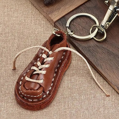 Brown leather shoe keychain with detailed stitching, laces, silver key ring and metal clip on textured fabric