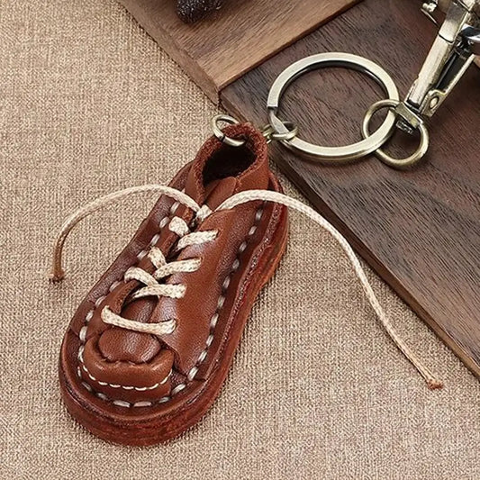Brown leather shoe keychain with detailed stitching, laces, silver key ring and metal clip on textured fabric
