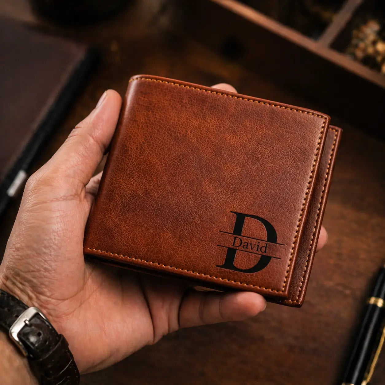 Leather Bifold Wallet in pebbled full-grain leather being held, showcasing a custom laser-engraved monogram and RFID security.