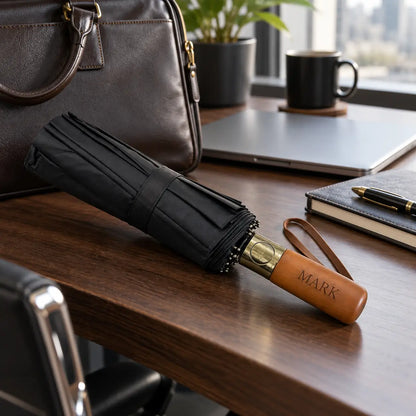 Personalised black folding umbrella with wooden handle engraved Mark on office desk with laptop and briefcase