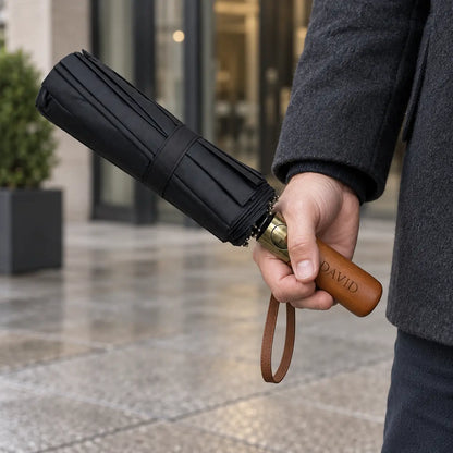 Man holding personalised black folding umbrella with wooden handle engraved David and brown wrist strap