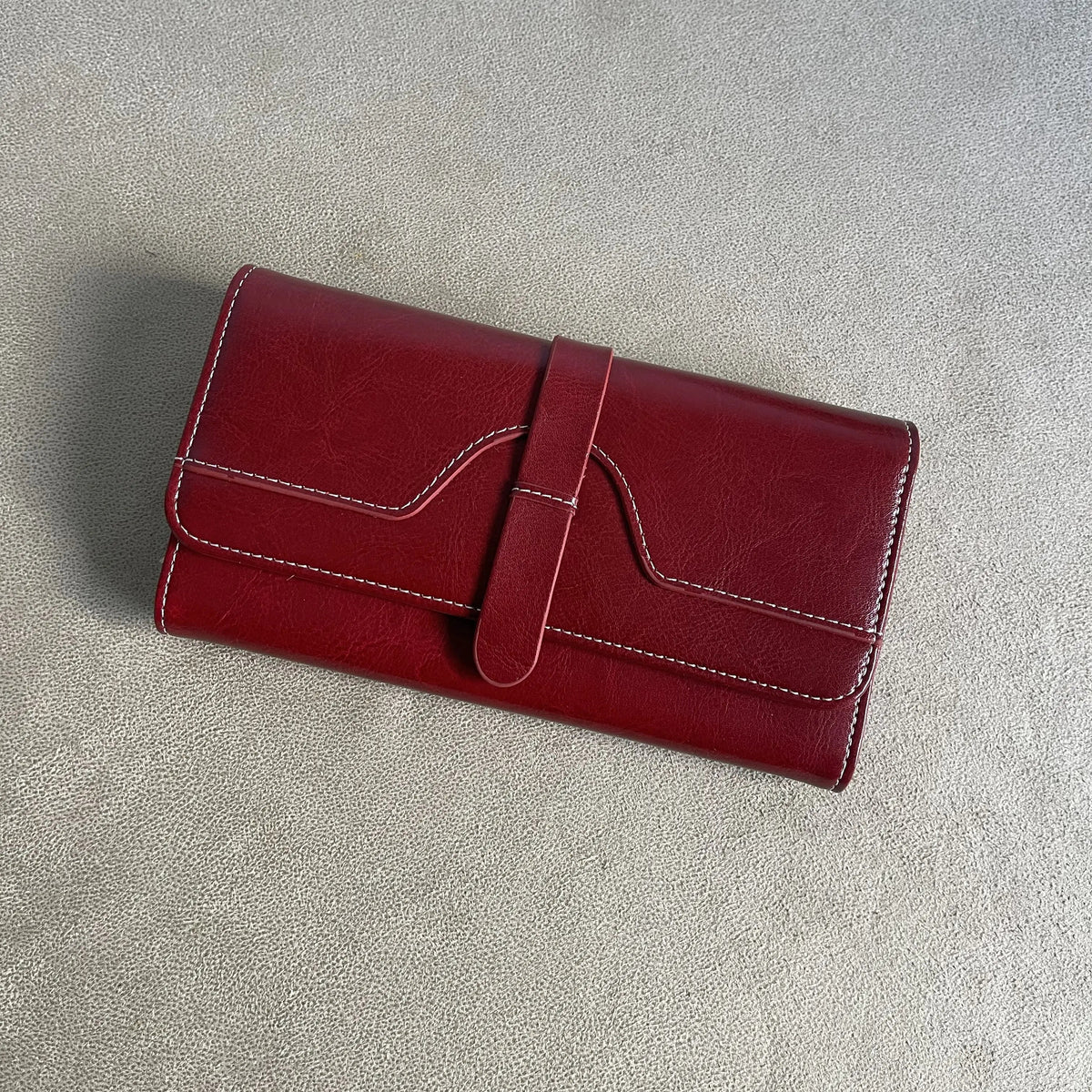 Burgundy red women’s long wallet with front strap closure, white contrast stitching and textured finish