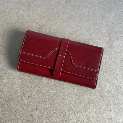 Burgundy red women’s long wallet with front strap closure, white contrast stitching and textured finish