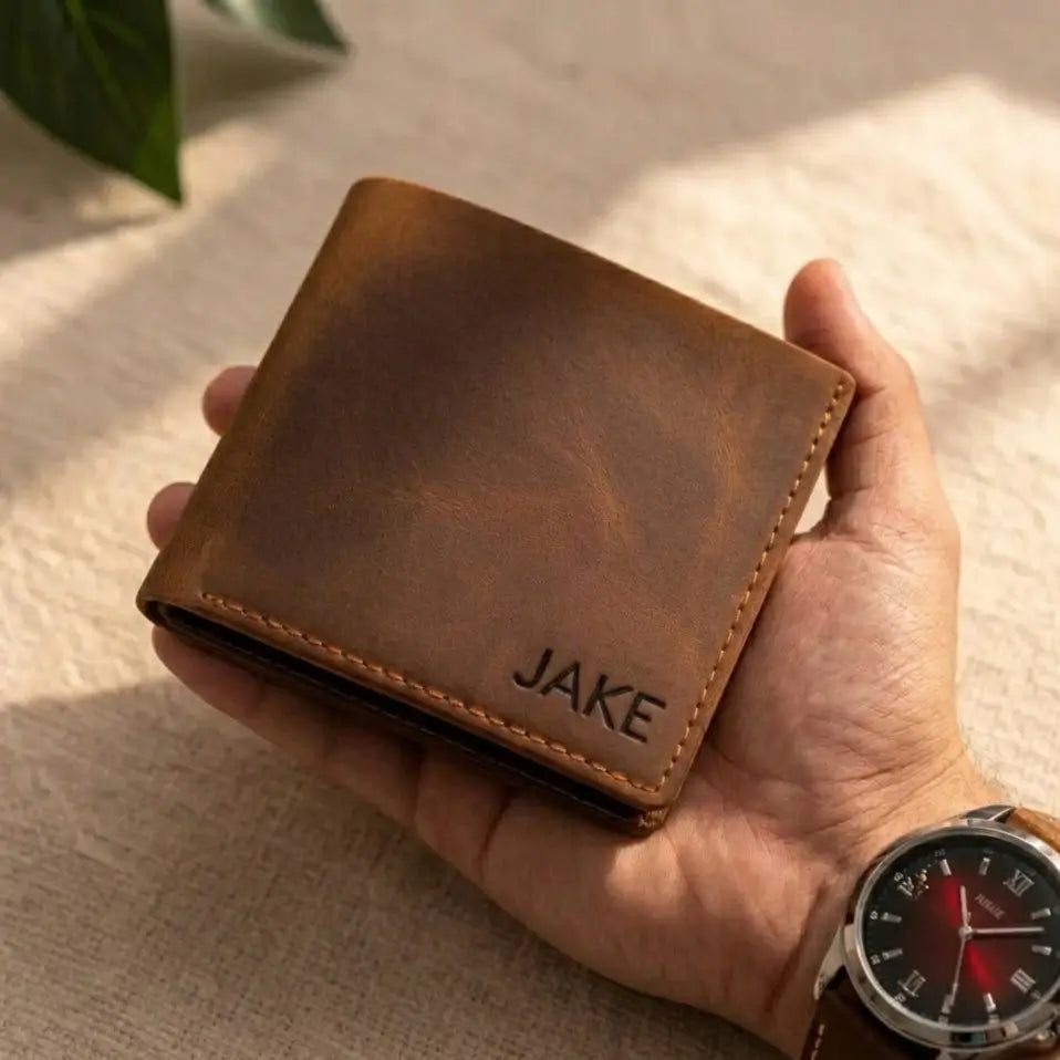 Leather Bifold Wallet in chestnut full-grain leather being held, featuring custom name engraving and hand-stitched detailing.