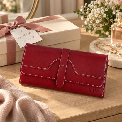 Personalised burgundy women’s wallet engraved with KIM displayed beside gift box, jewellery and flowers