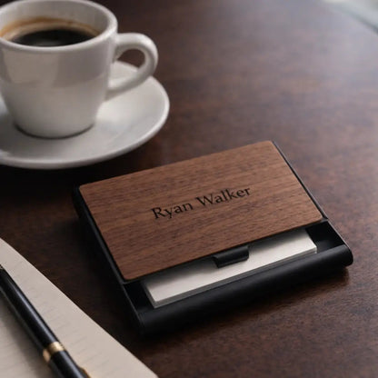 Custom wooden business card holder engraved with “Ryan Walker” displayed on a wooden coffee table beside a cup of coffee, notebook, and pen with a clean minimalist office aesthetic.