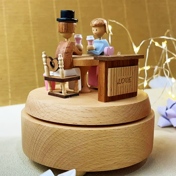 A wooden couple figurine sharing coffee, featured on a decorative music box, used as a charming gift or collectible item.