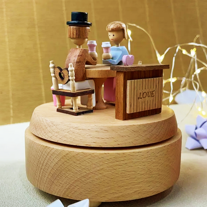 A wooden couple figurine sharing coffee, featured on a decorative music box, used as a charming gift or collectible item.